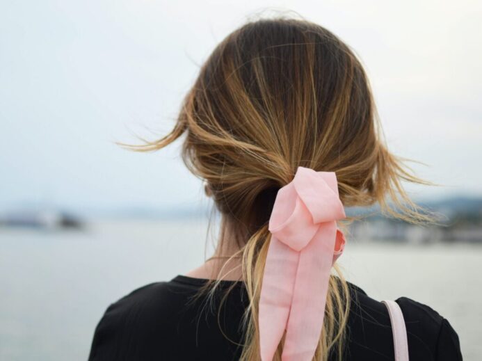 focus photography of woman with pink hair bow facing on body of water