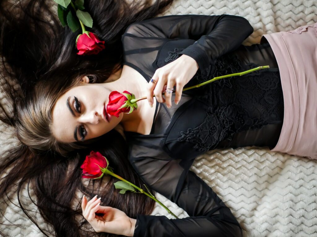 woman lying on white bed holding red rose