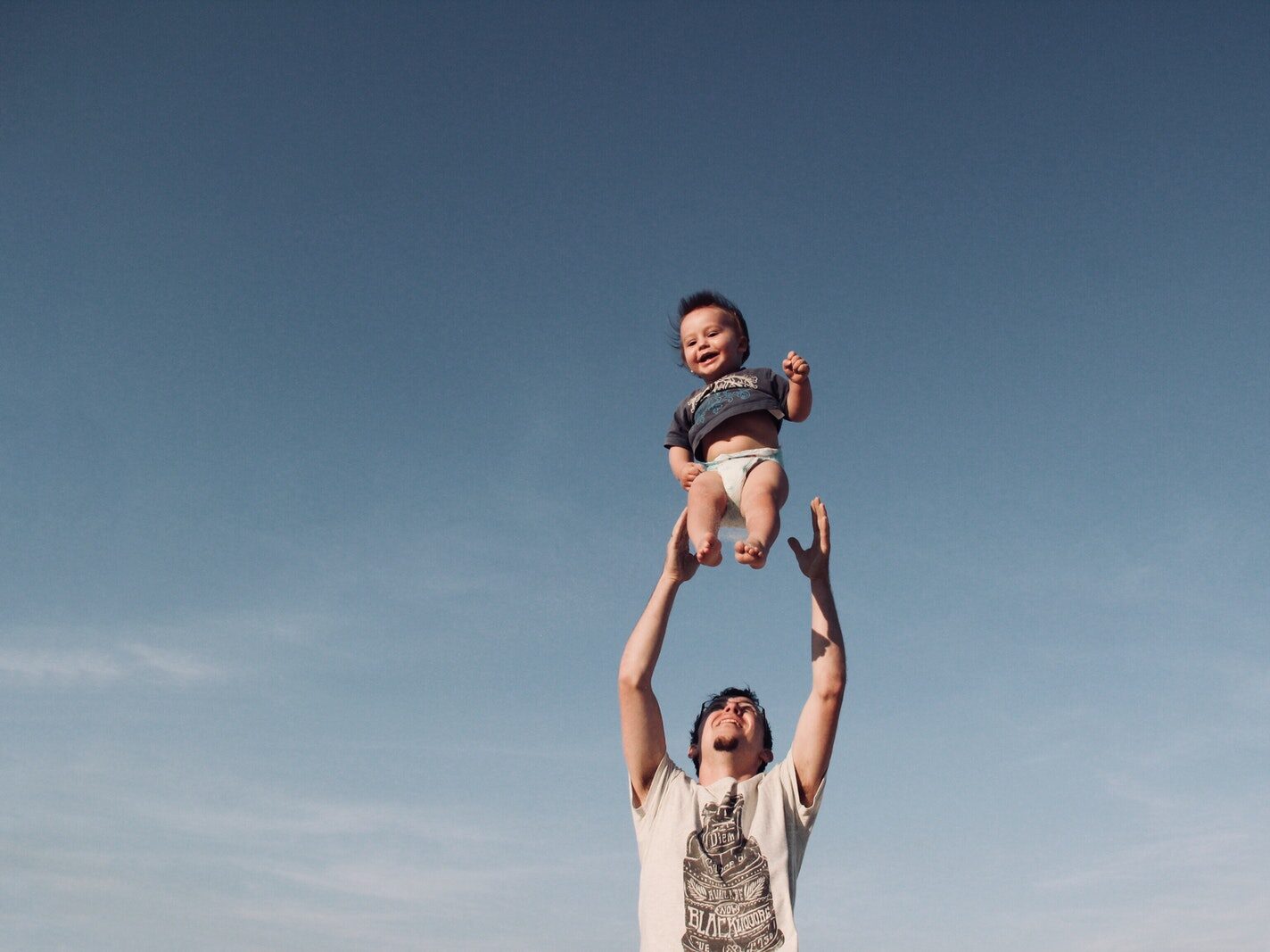 Photo of Man in Raising Baby Under Blue Sky