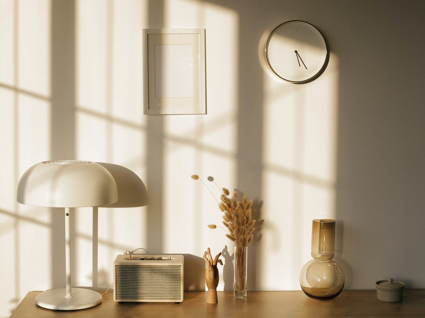 Light room with retro radio and decorative vases with dry plants on desk near wall with clock and window shadow in sunlight