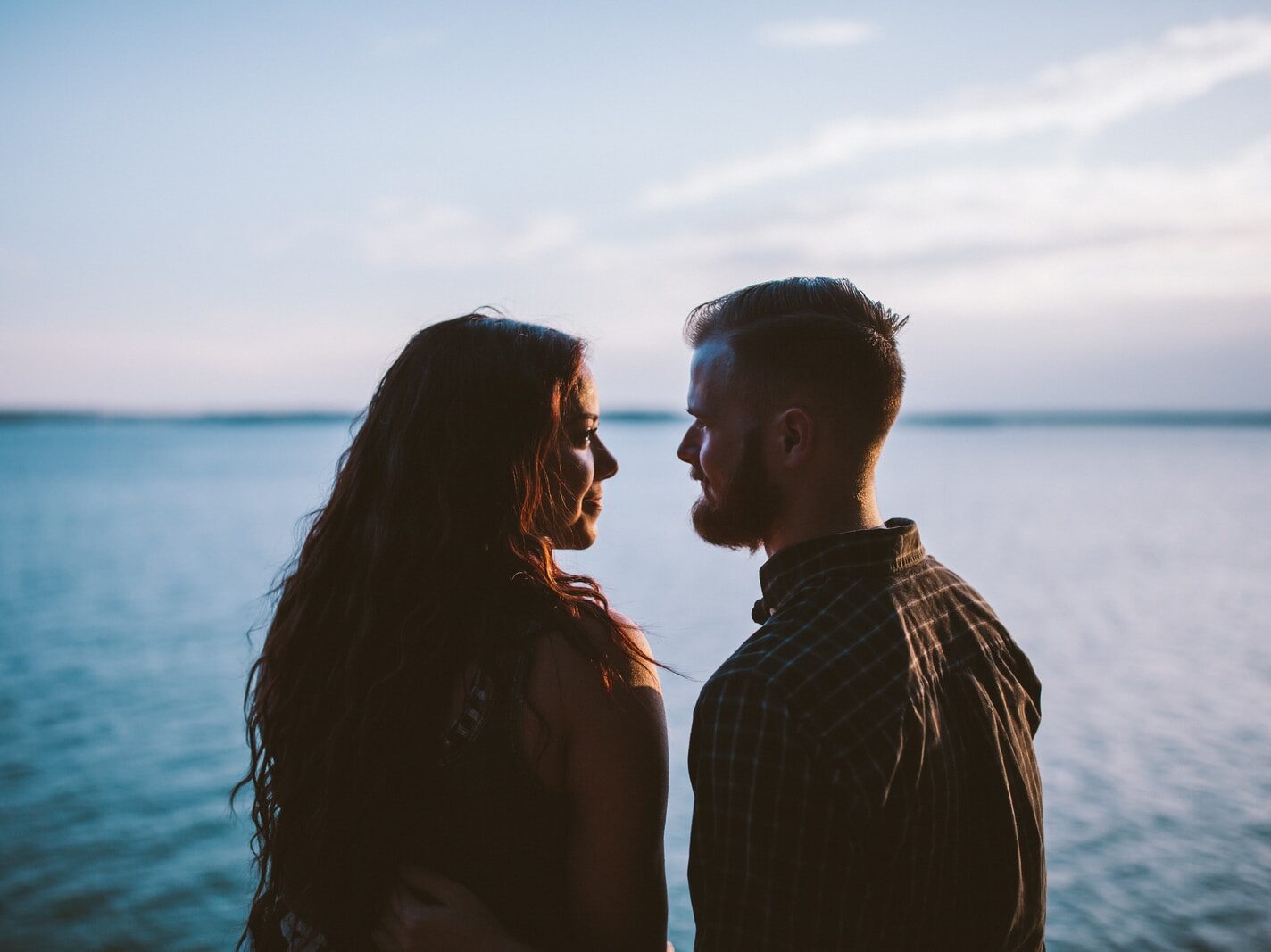 man and woman standing while looking each other near body of water