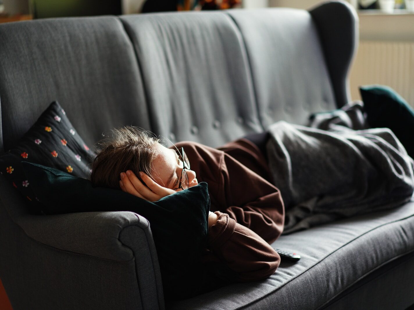 woman in pink jacket lying on gray couch