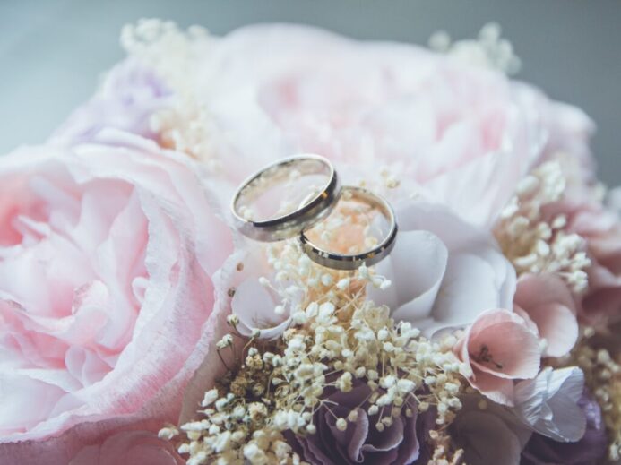gold-colored bridal ring set on pink rose flower bouquet