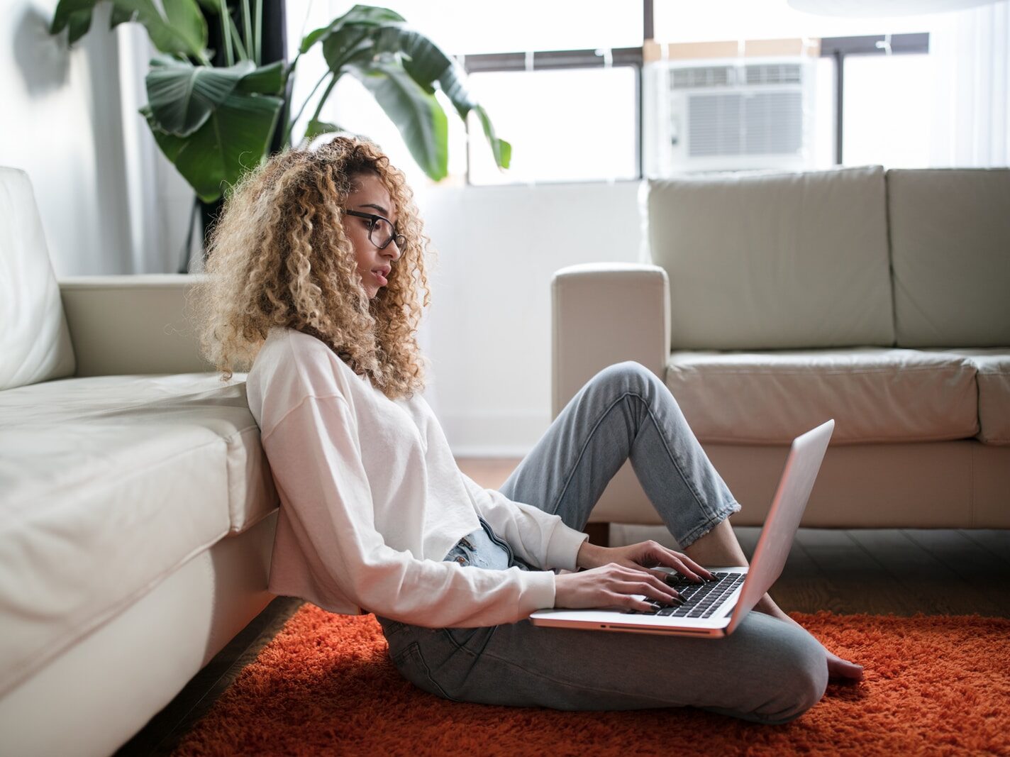 woman sitting on floor and leaning on couch using laptop