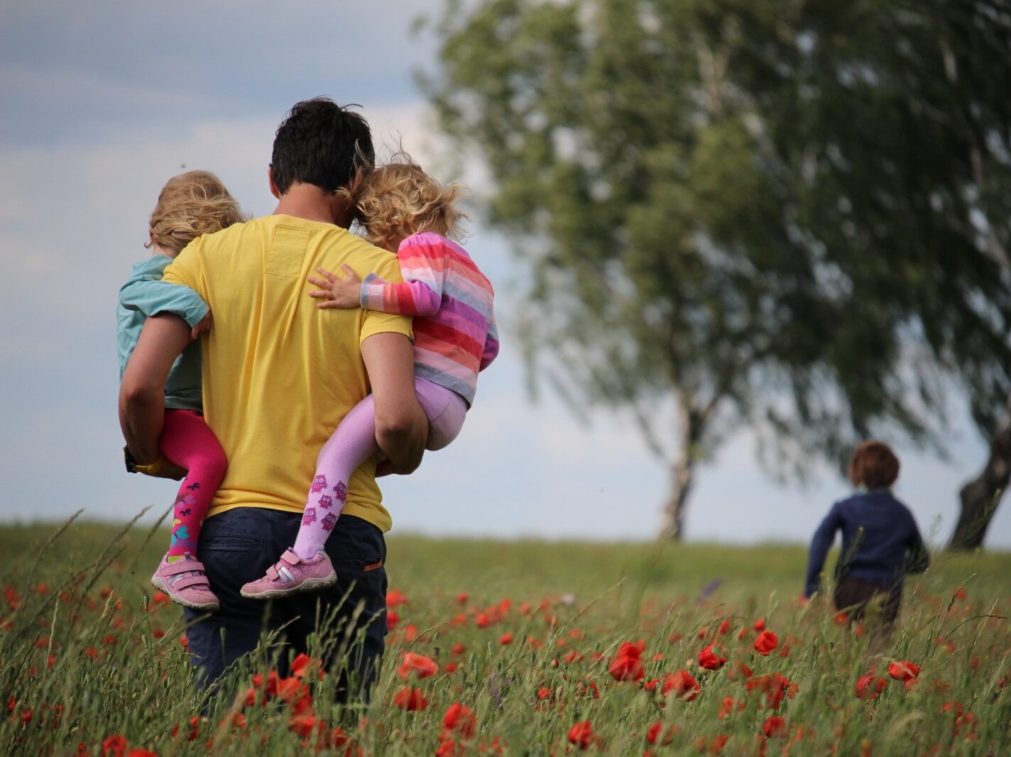 man carrying to girls on field of red petaled flower