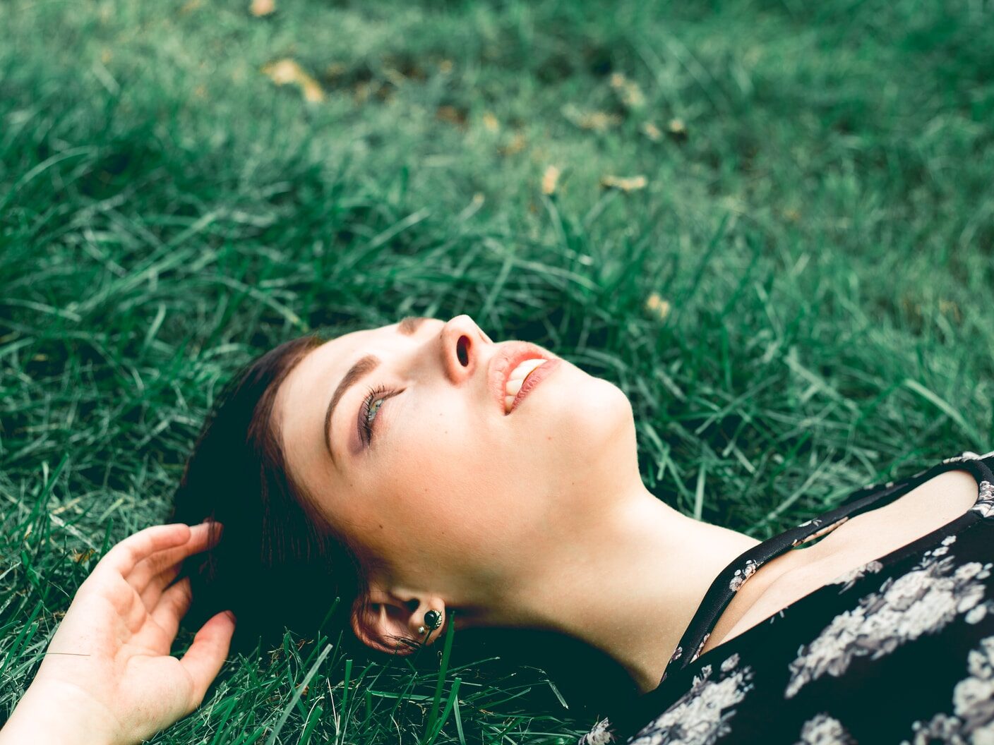 woman in black and white floral shirt lying on green grass field