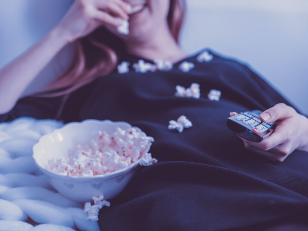 woman lying on bed while eating puff corn