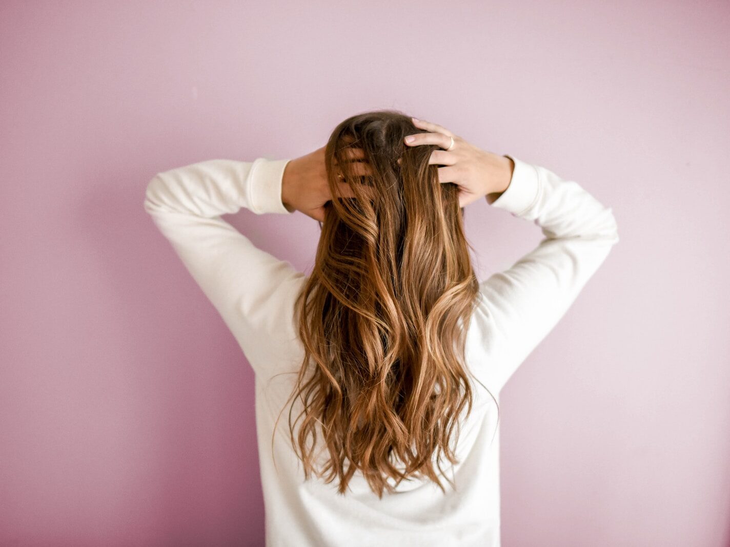 woman in white long-sleeved shirt standing in front of pink wall