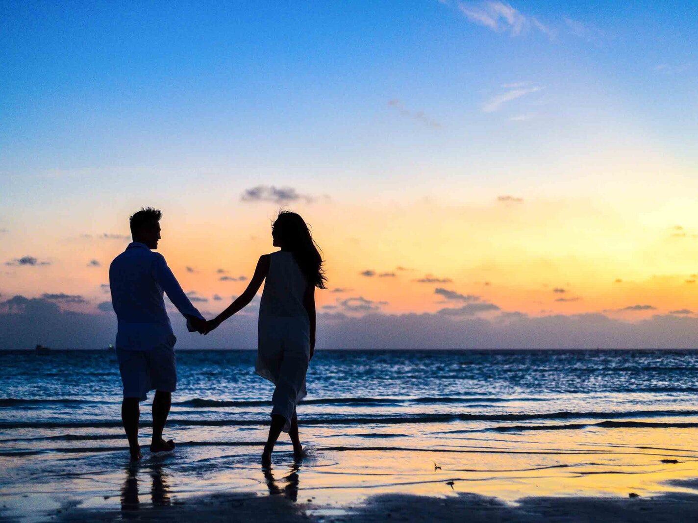 Man and Woman Holding Hands Walking on Seashore during Sunrise