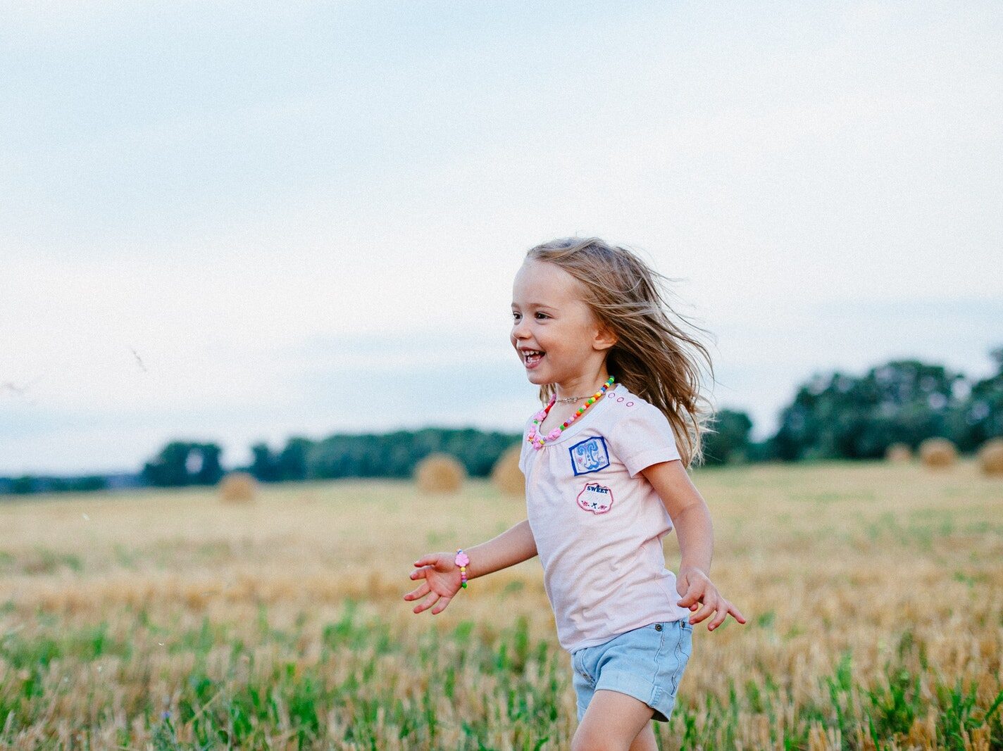 Smiling Girl Running Towards Left on Green Field