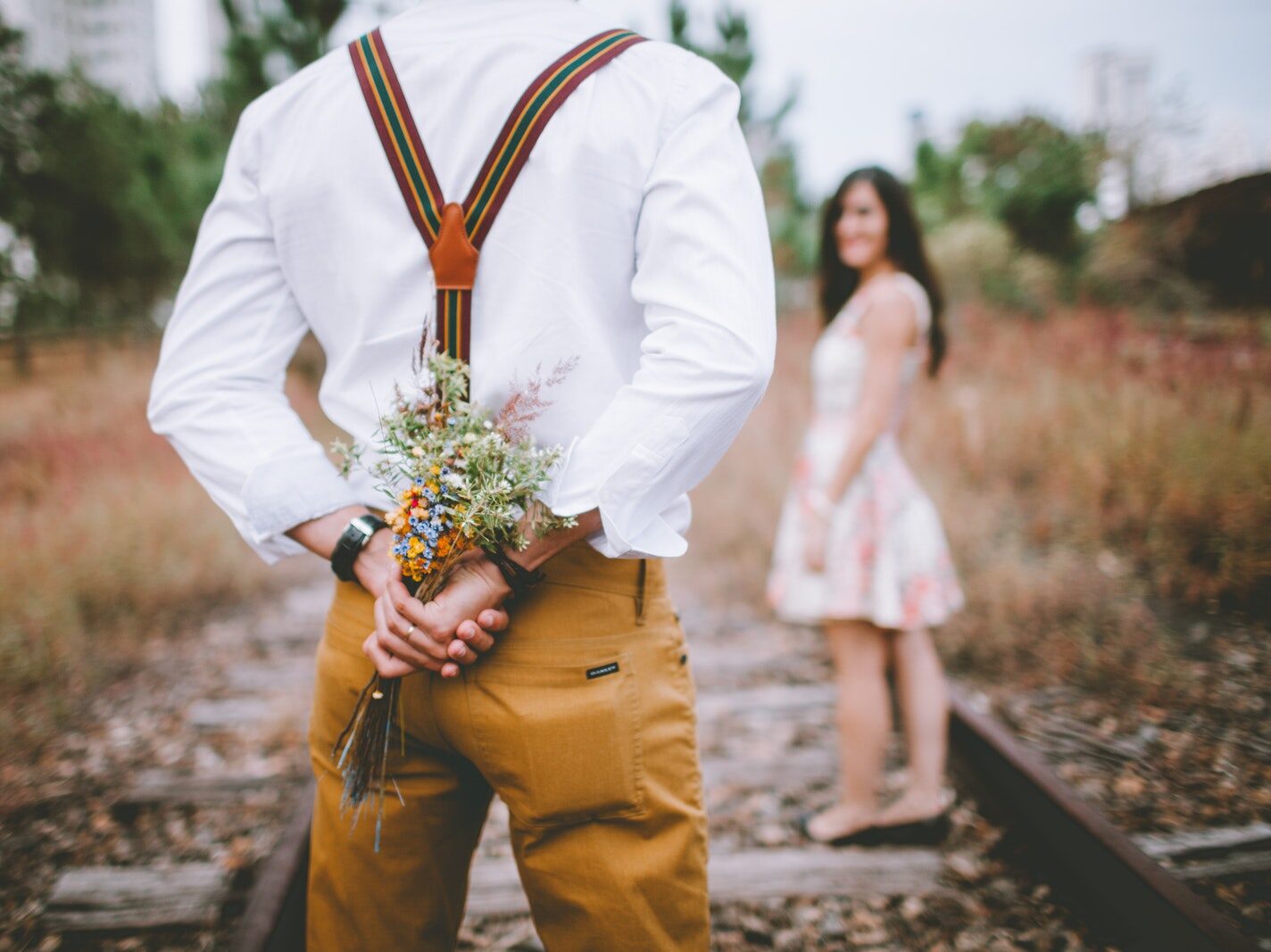 Man Holding Flowers Standing Beside Woman on Railroad
