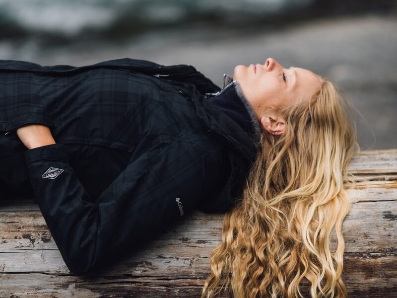 woman in black zip-up jacket leaning on large log at daytime