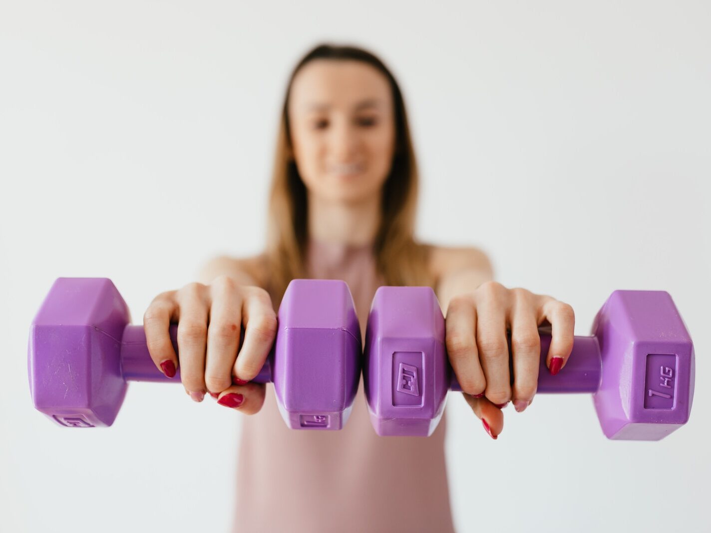 Defocused content young female doing bicep exercise with dumbbells during functional training in light studio