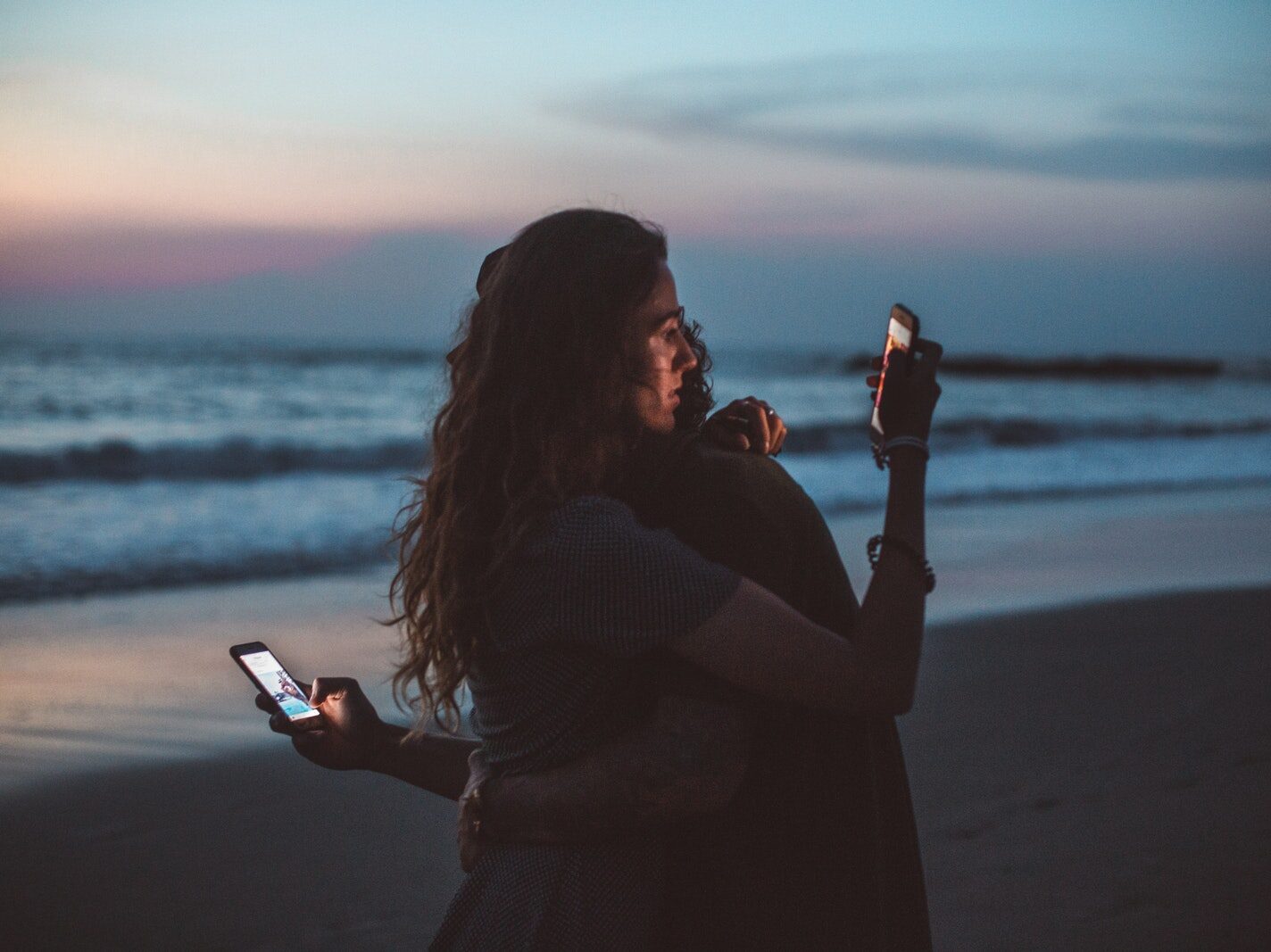 Couple hugging and using smartphone near sea on sunset