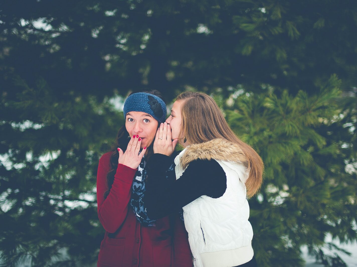 woman whispering on woman's ear while hands on lips