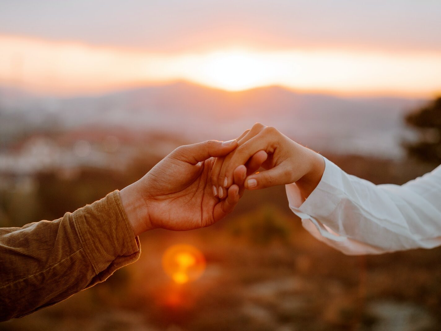 Unrecognizable couple holding hands at sunset