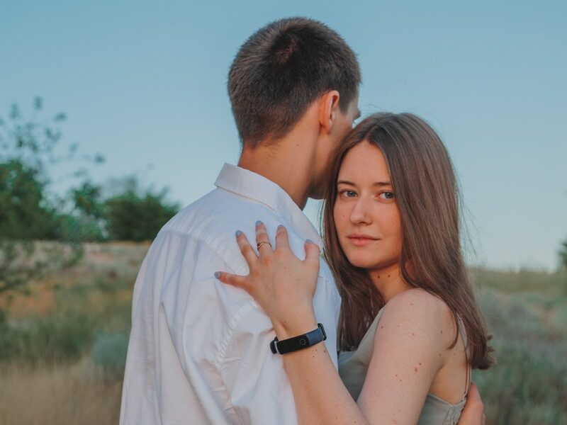 Content woman embracing anonymous man while standing on sandy road in countryside against blue sky in summer day in nature