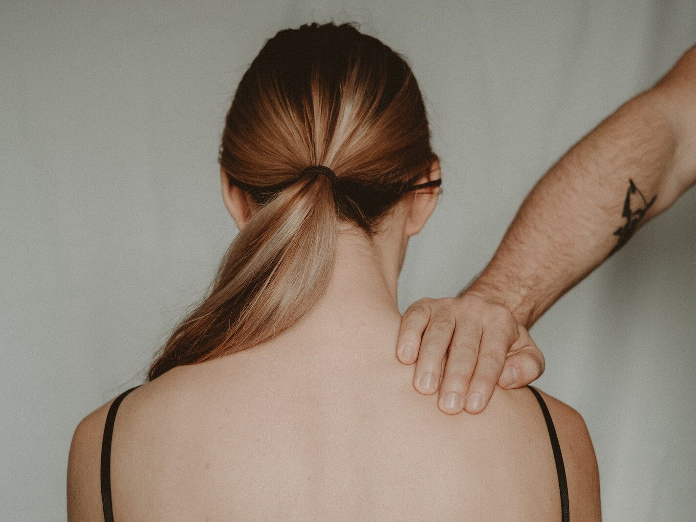 Back view of anonymous female sitting on white background while being touched by strong faceless abusive man in light room
