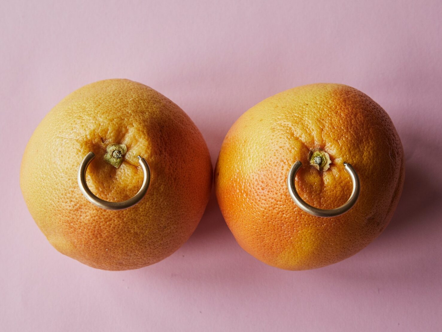 Fresh mandarins with earrings placed on pink surface