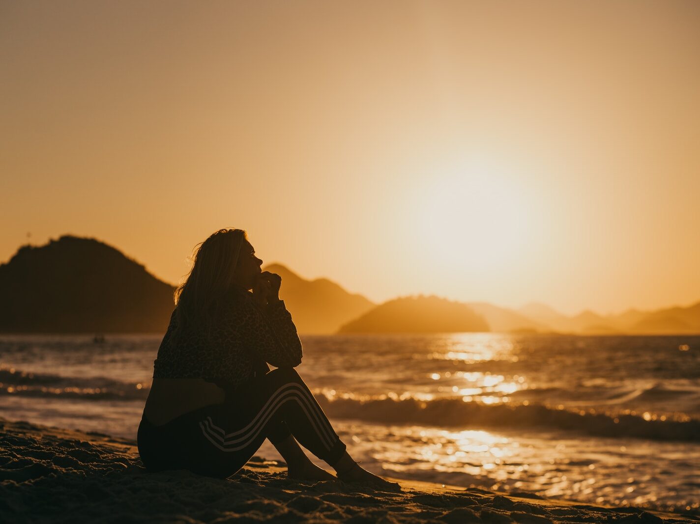 silhouette of woman sitting on beach during sunset