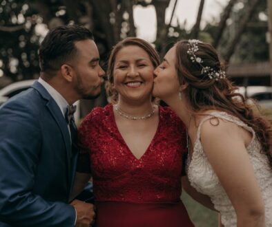 Ethnic bride and groom kissing smiling mom in elegant wear during festive event in countryside
