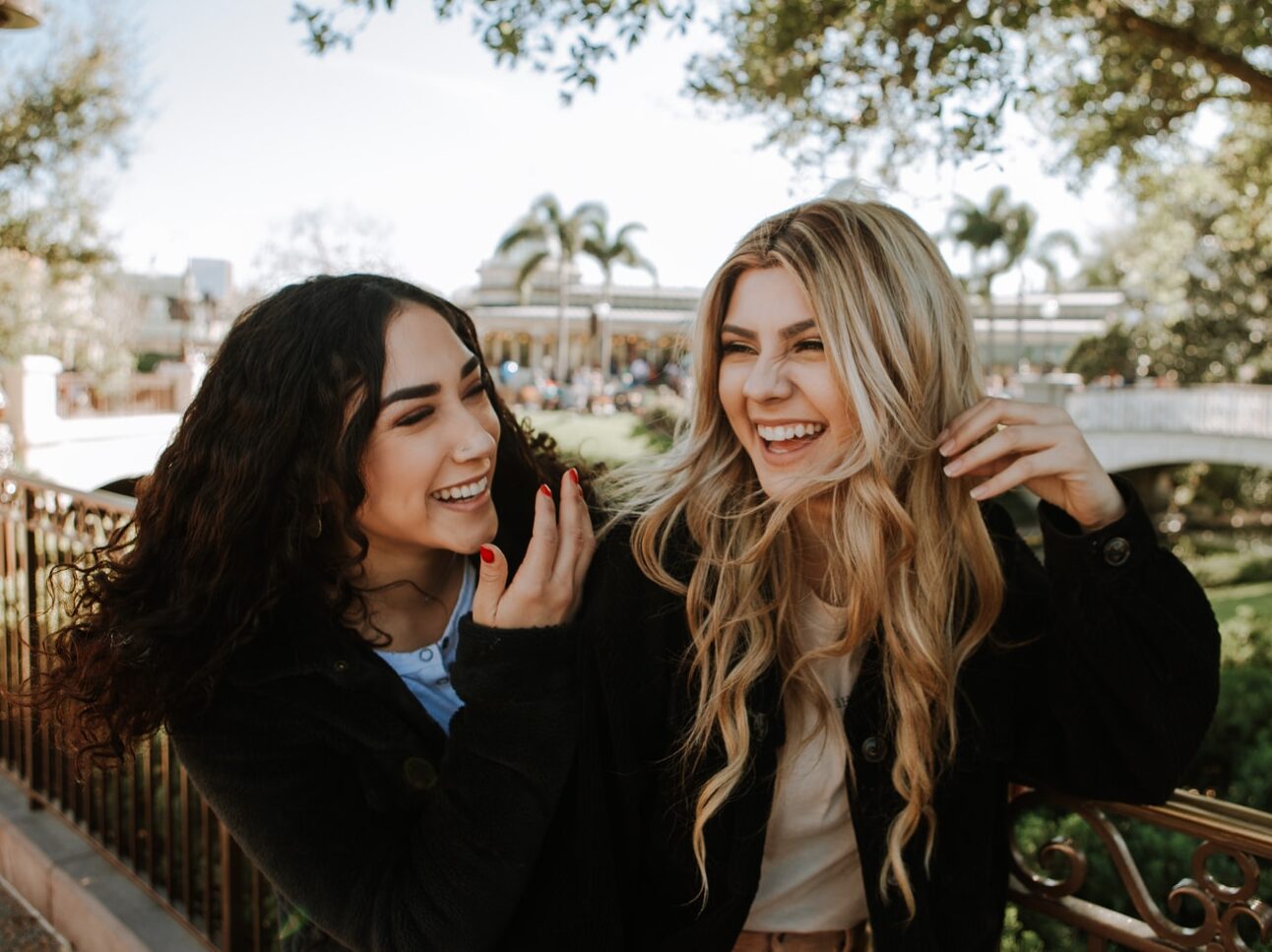 2 women smiling and standing near trees during daytime