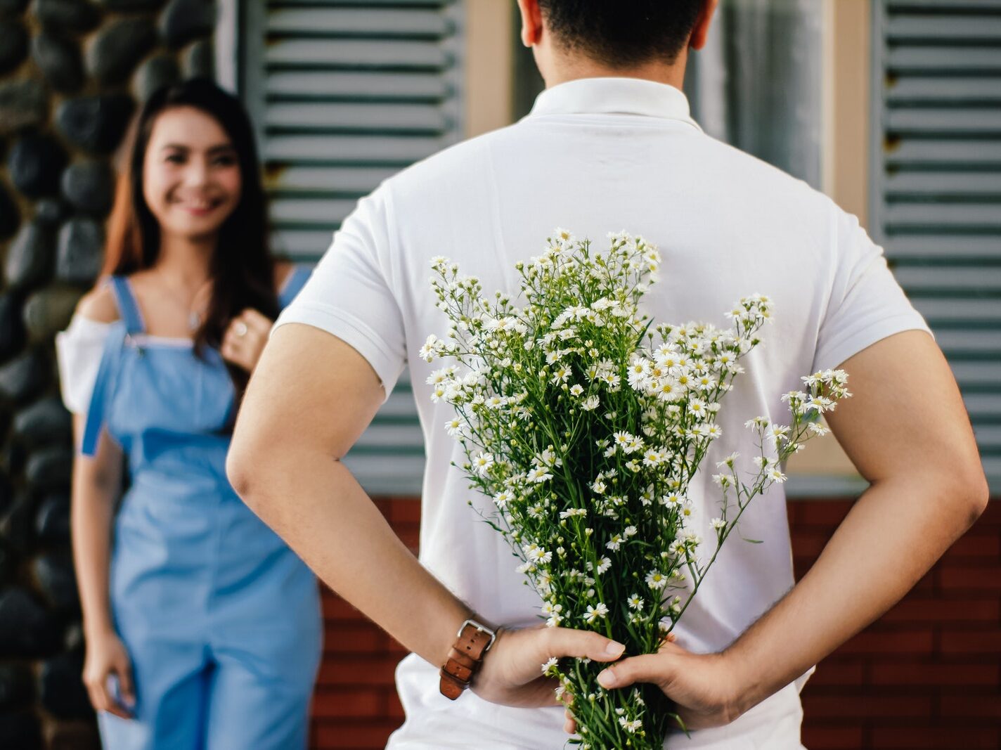Man Holding Baby's-breath Flower in Front of Woman Standing Near Marble Wall