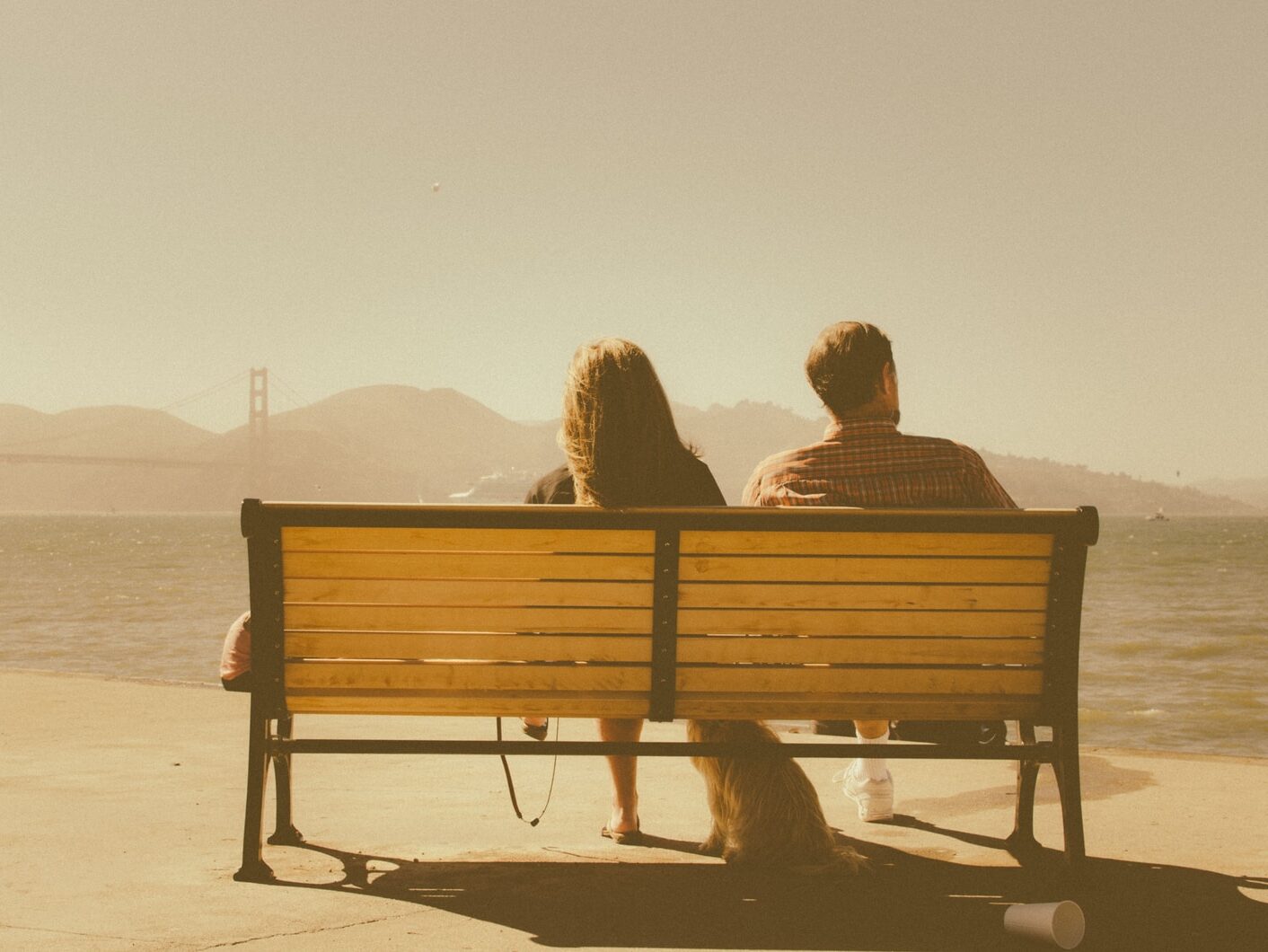 man and woman sitting on bench beside body of water