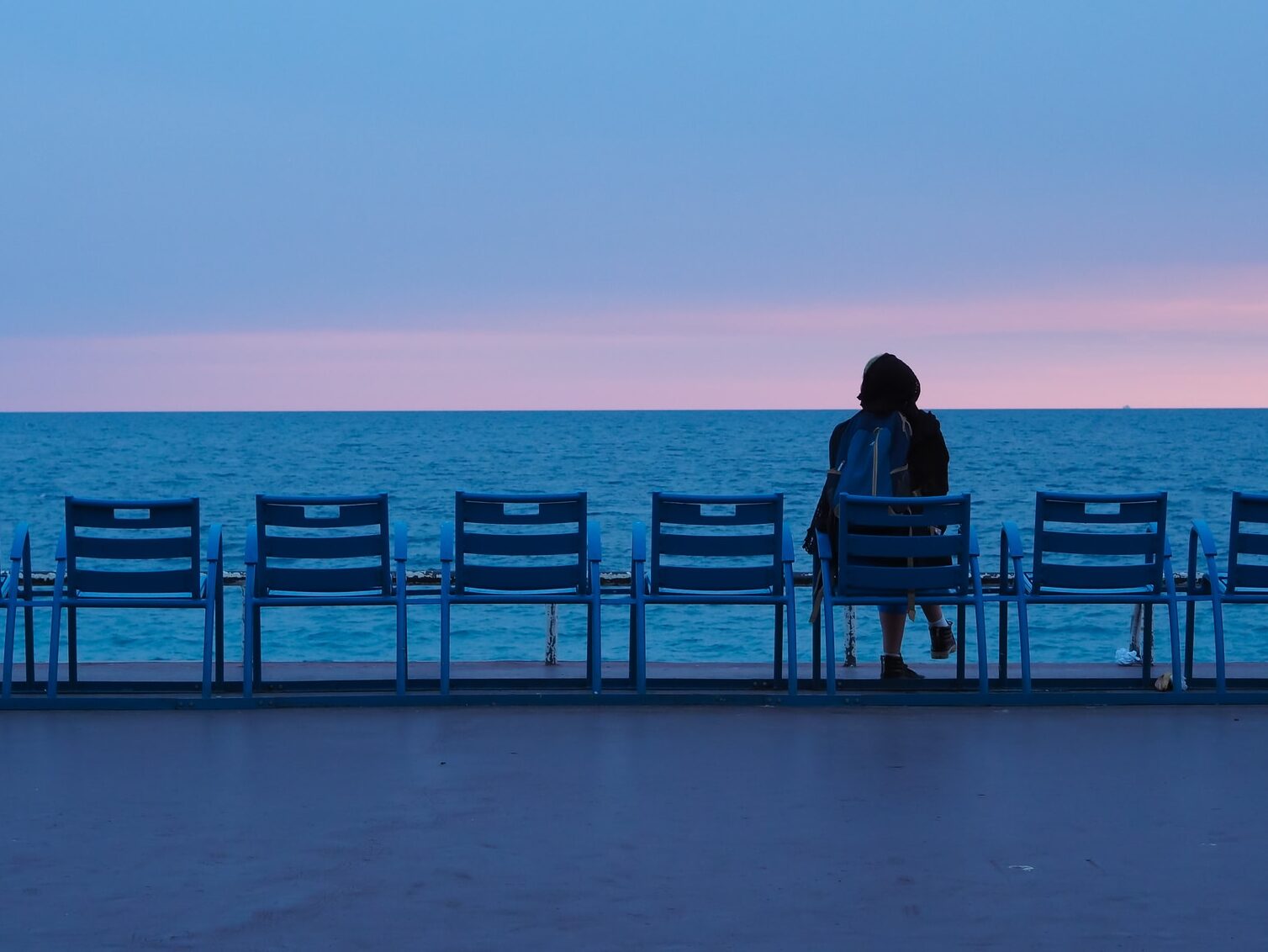 person sitting on blue wooden bench on beach during daytime