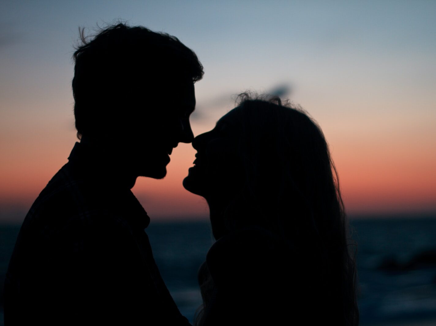 silhouette of man and woman about to kiss on beach during sunset