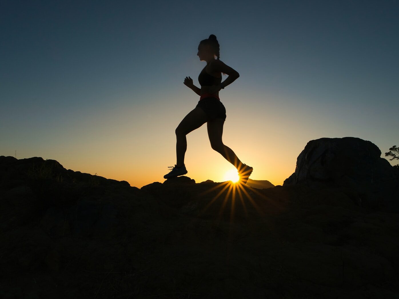 silhouette of man jumping on rocky mountain during sunset