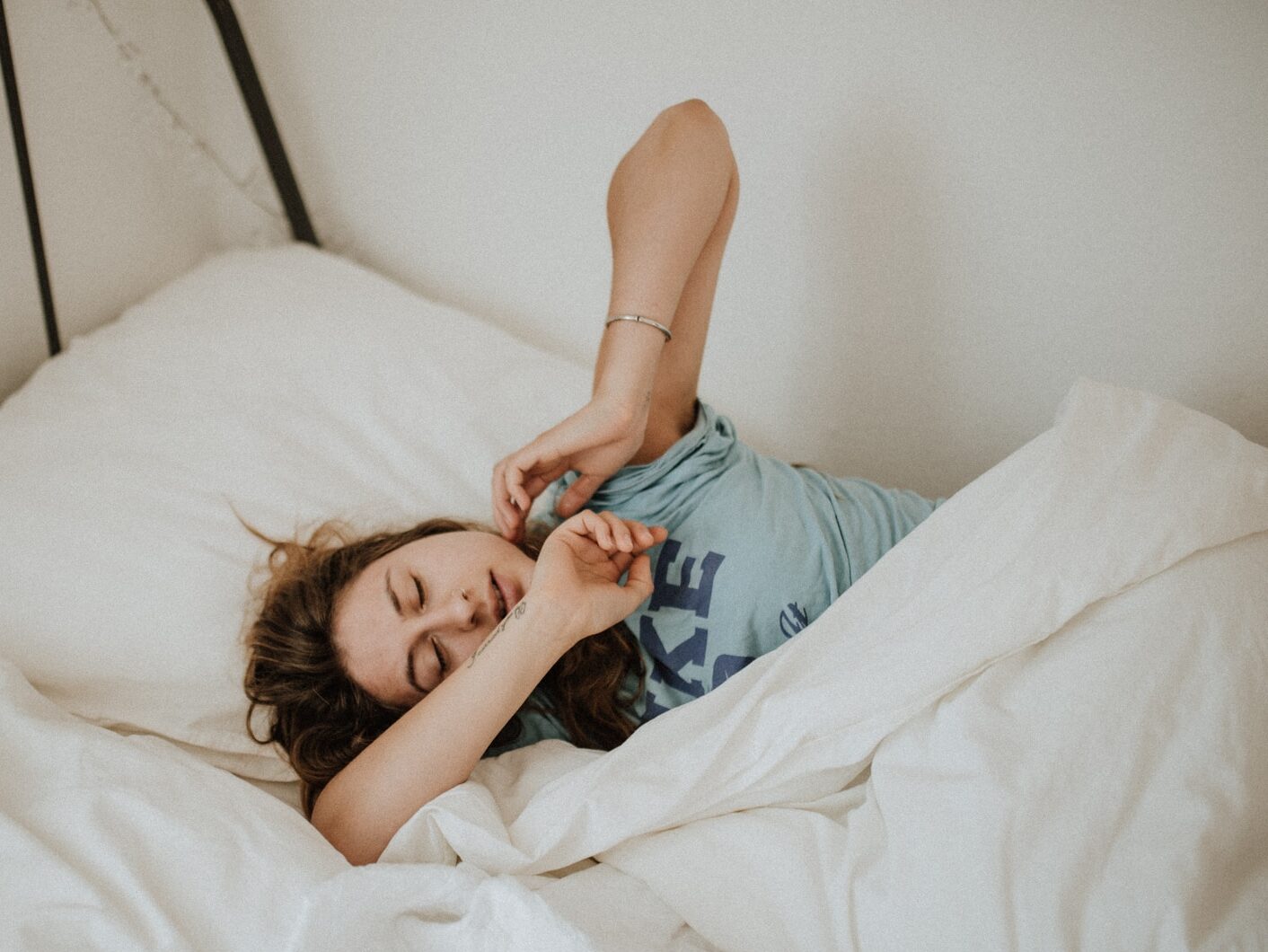 woman covered in white blanket sleeping on white bed comforter