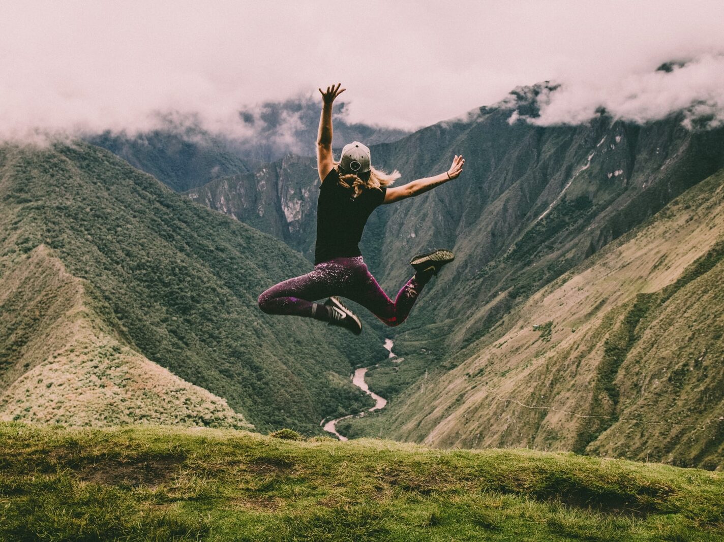 woman jumping on green mountains