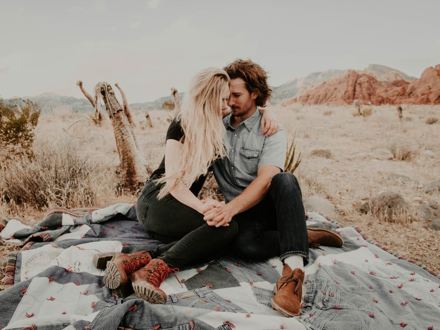man and woman sitting on blanket while holding each other hands