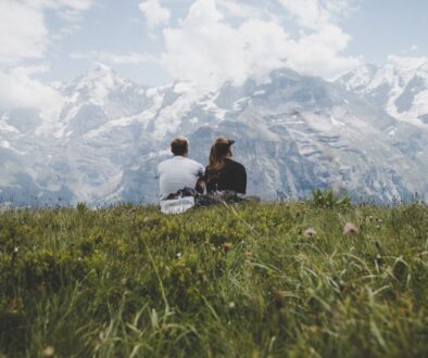 man sitting beside woman on grass facing mountains