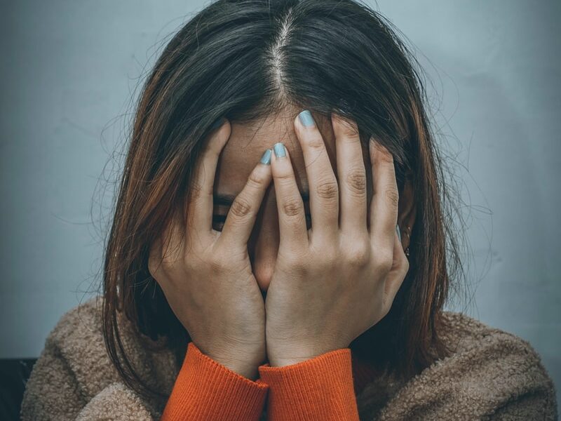 woman in brown sweater covering her face with her hand