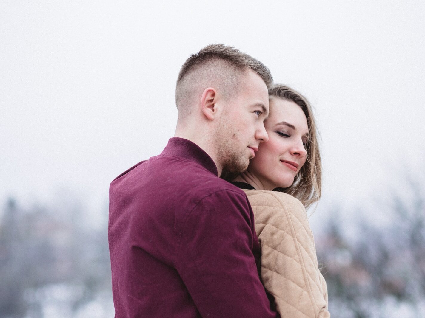 man hugging woman while standing on snowy weather