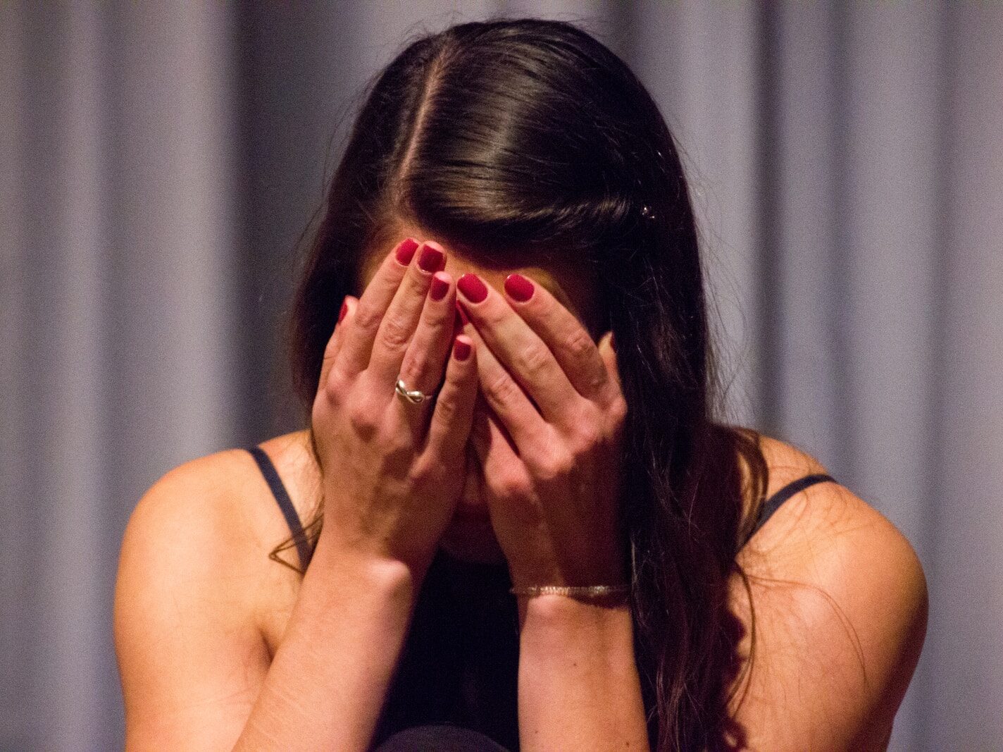 woman in black tank top covering her face with her hands