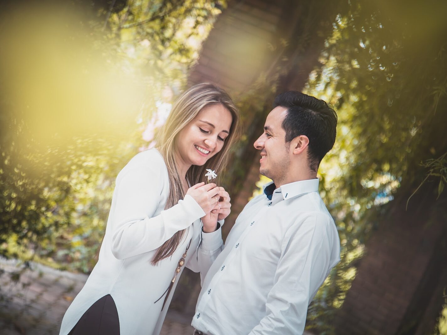 man giving white flower to woman surrounded by green trees
