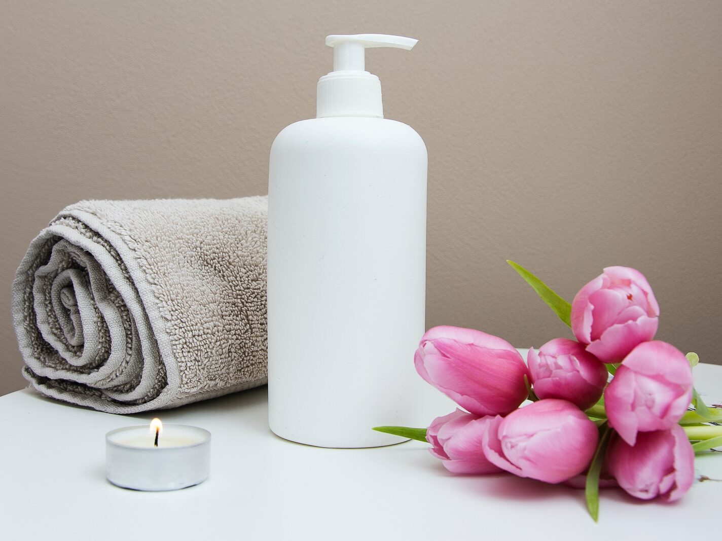 white plastic pump bottle beside pink tulips and gray towel