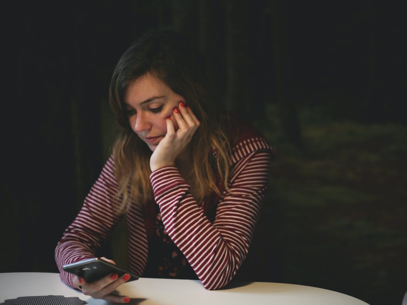 woman leaning on white wooden table while holding black Android smartphone