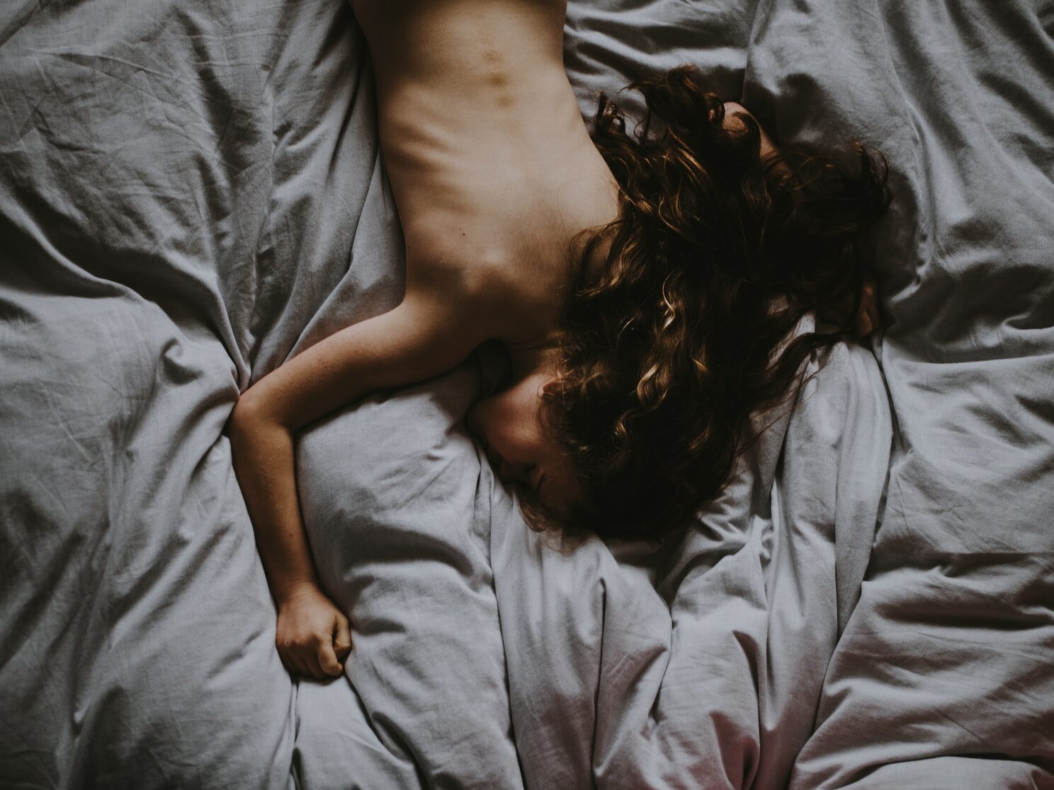 naked woman lying on gray bedspread