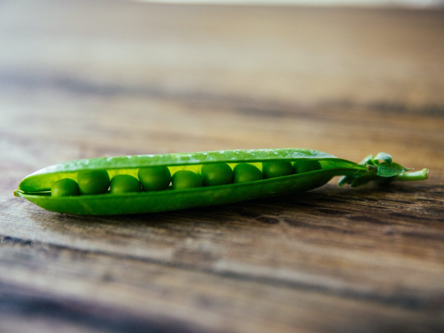 shallow focus photography of green pea on brown wooden surface
