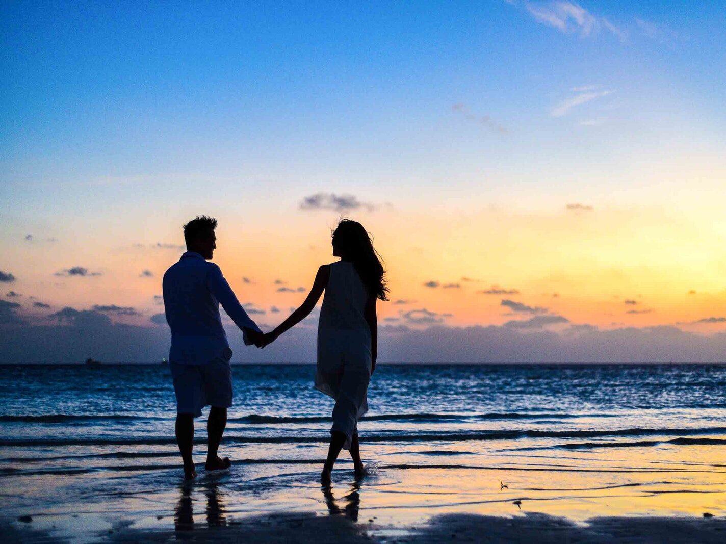 Man and Woman Holding Hands Walking on Seashore during Sunrise