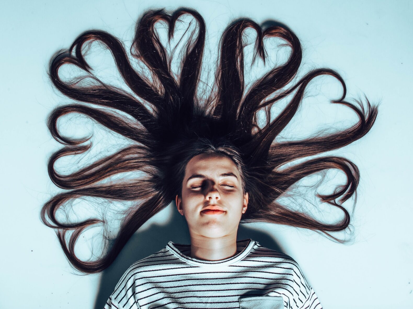 woman laying on white surface with heart forming hair