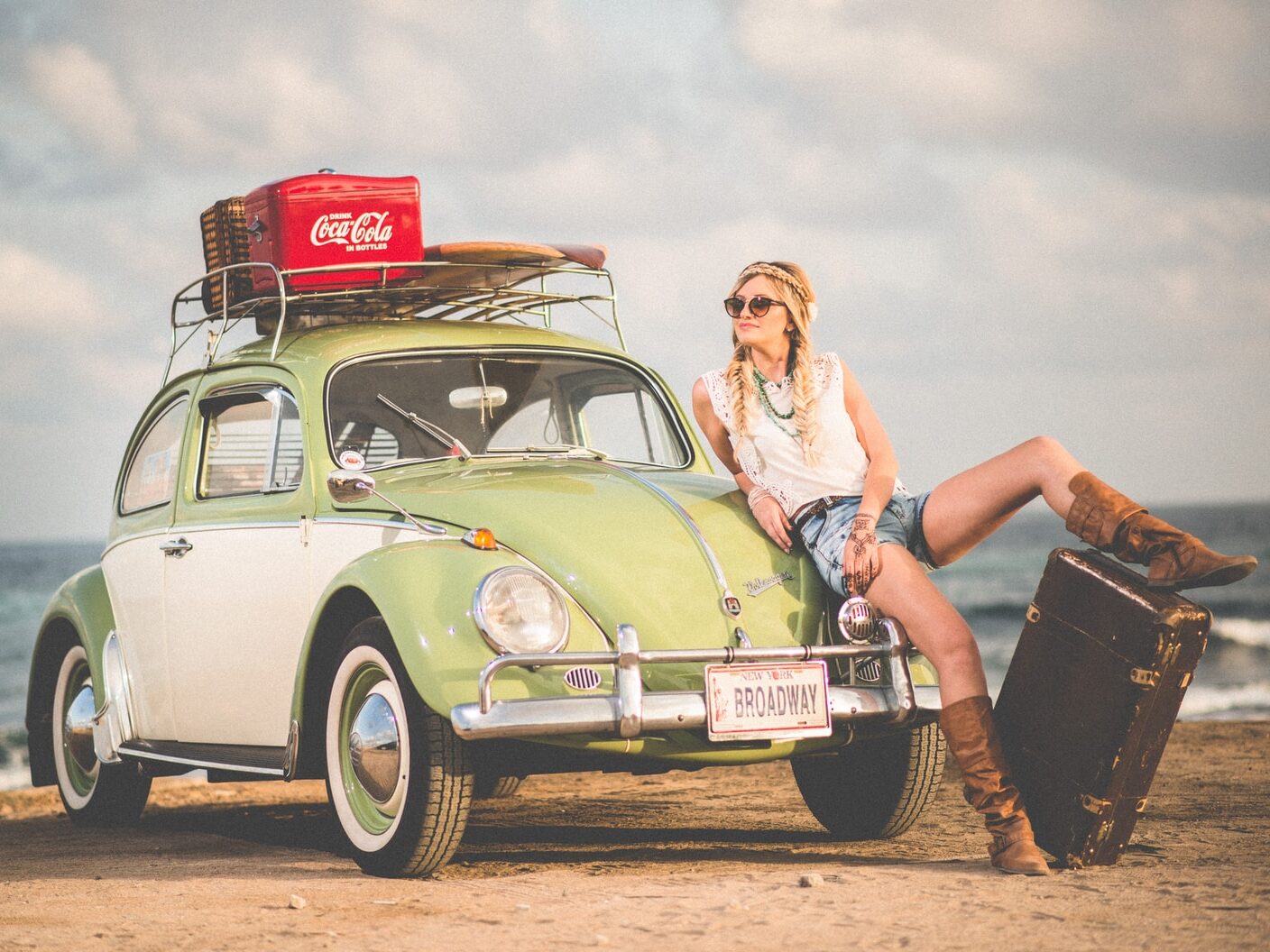 woman leaning on green and white Volkswagen Beetle near sea under white sky during daytime