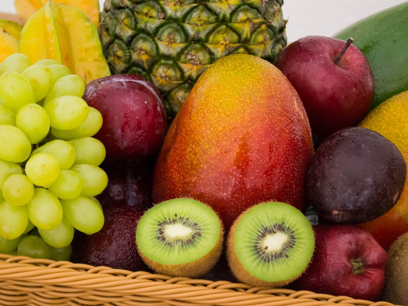 red apple fruit beside green apple and yellow fruit on brown woven basket