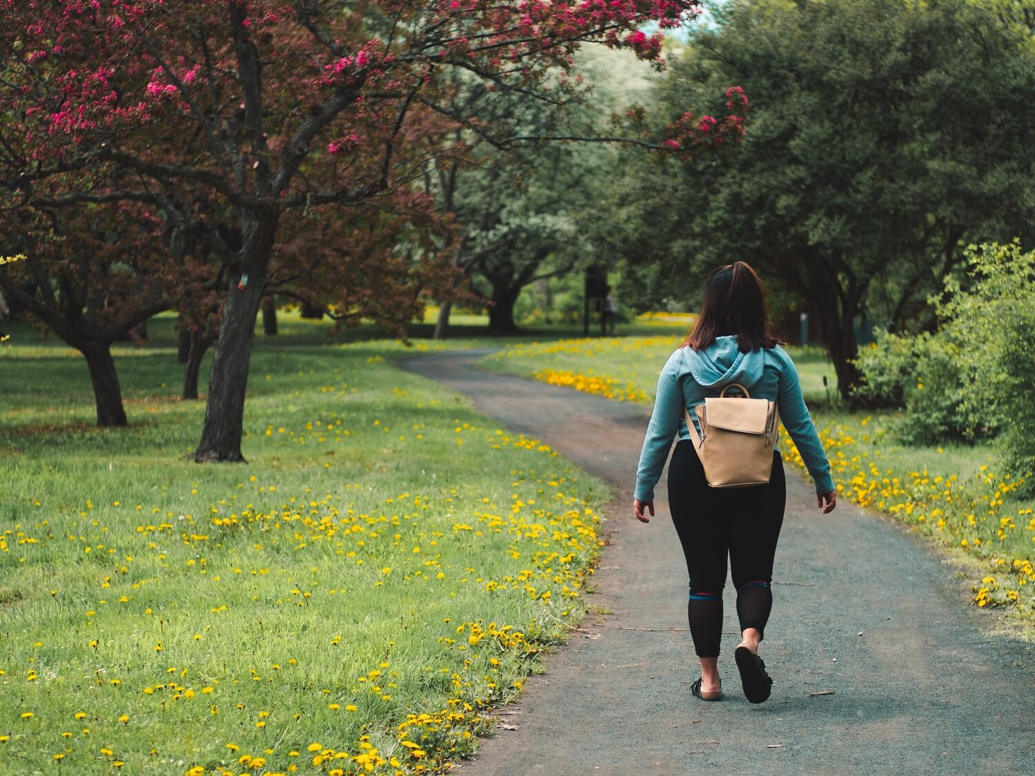 woman wearing blue jacket and black pants walking on grass field pathway