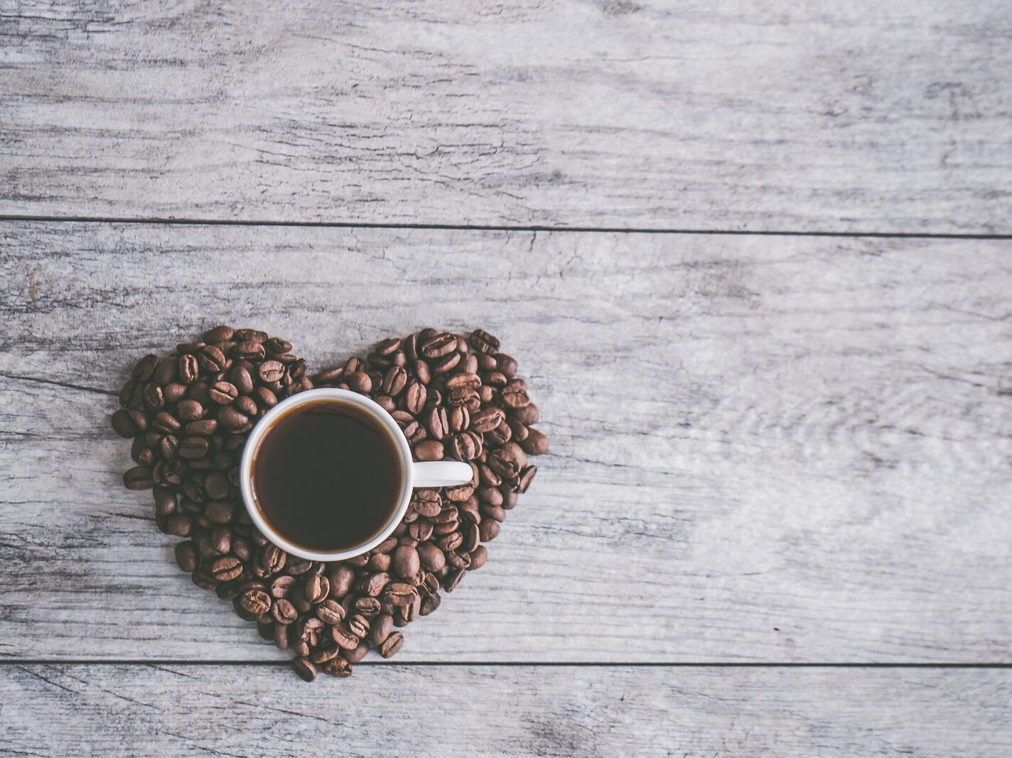 coffee filled white ceramic mug beside brown coffee beans on beige wooden surface