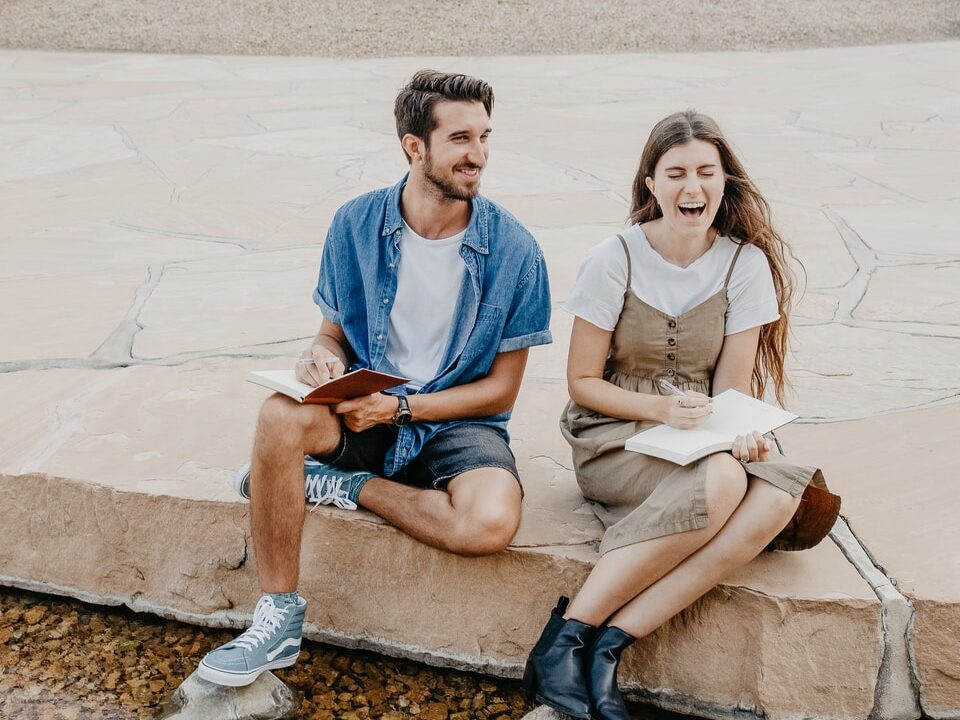 man and woman sitting side by side holding notebooks